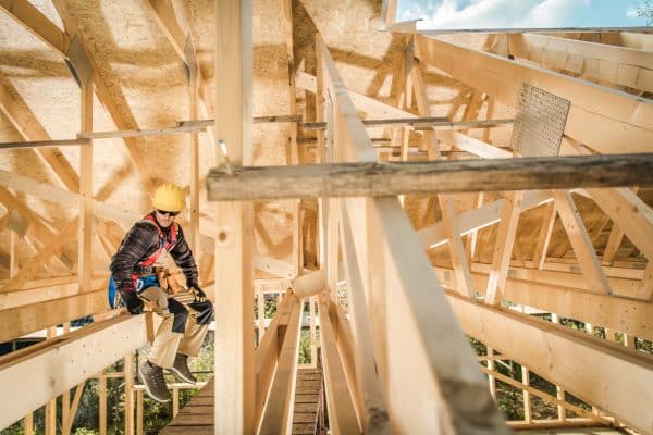 Ein Zimmermann arbeitet auf dem Gerüst an tragenden Elementen des Holzbaus.