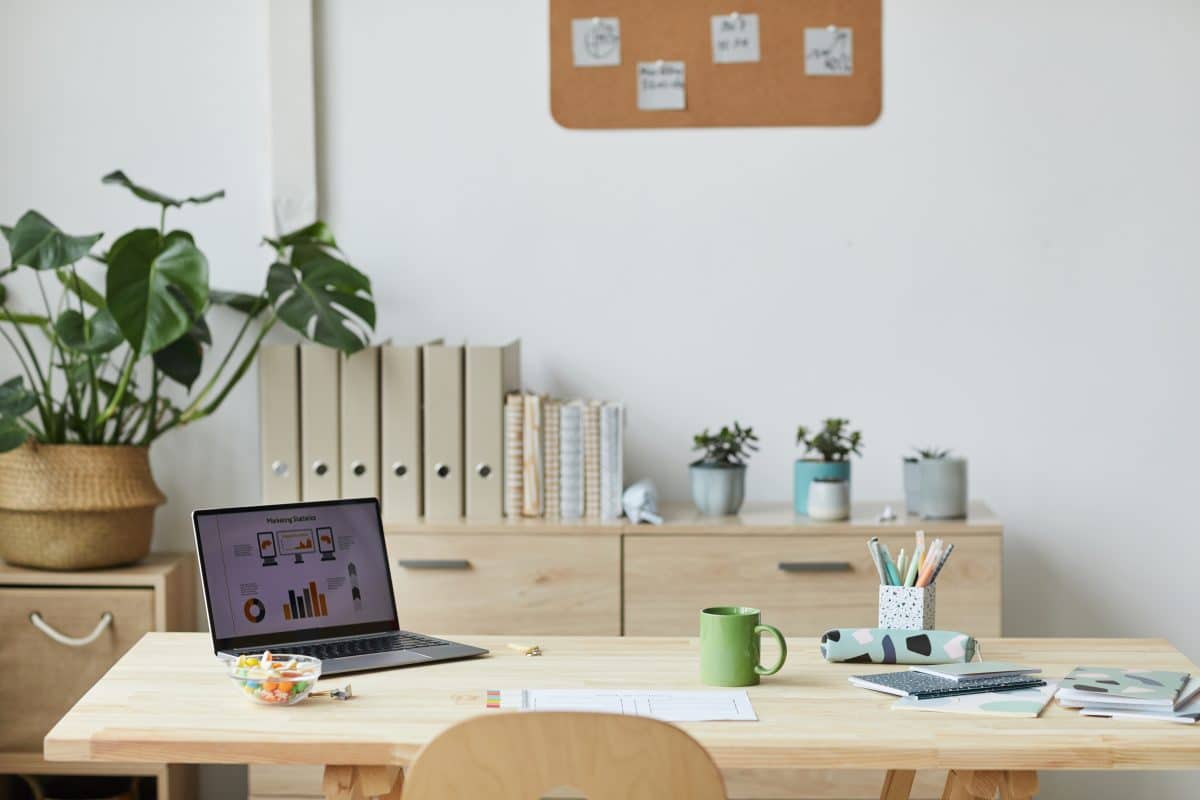 Minimalistischer Homeoffice-Platz mit Laptop, Pflanzen und Ordnern.