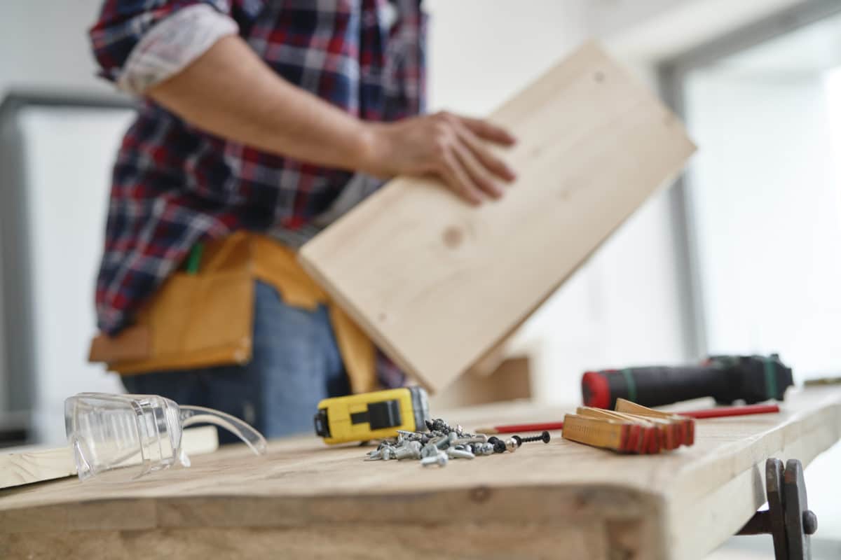 Heimwerker mit Holzplatte an Werkbank mit Werkzeugen.