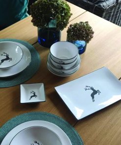 Gedeckter Eichenholztisch mit Geschirr im Hirschdesign und blauer Tischdekoration.