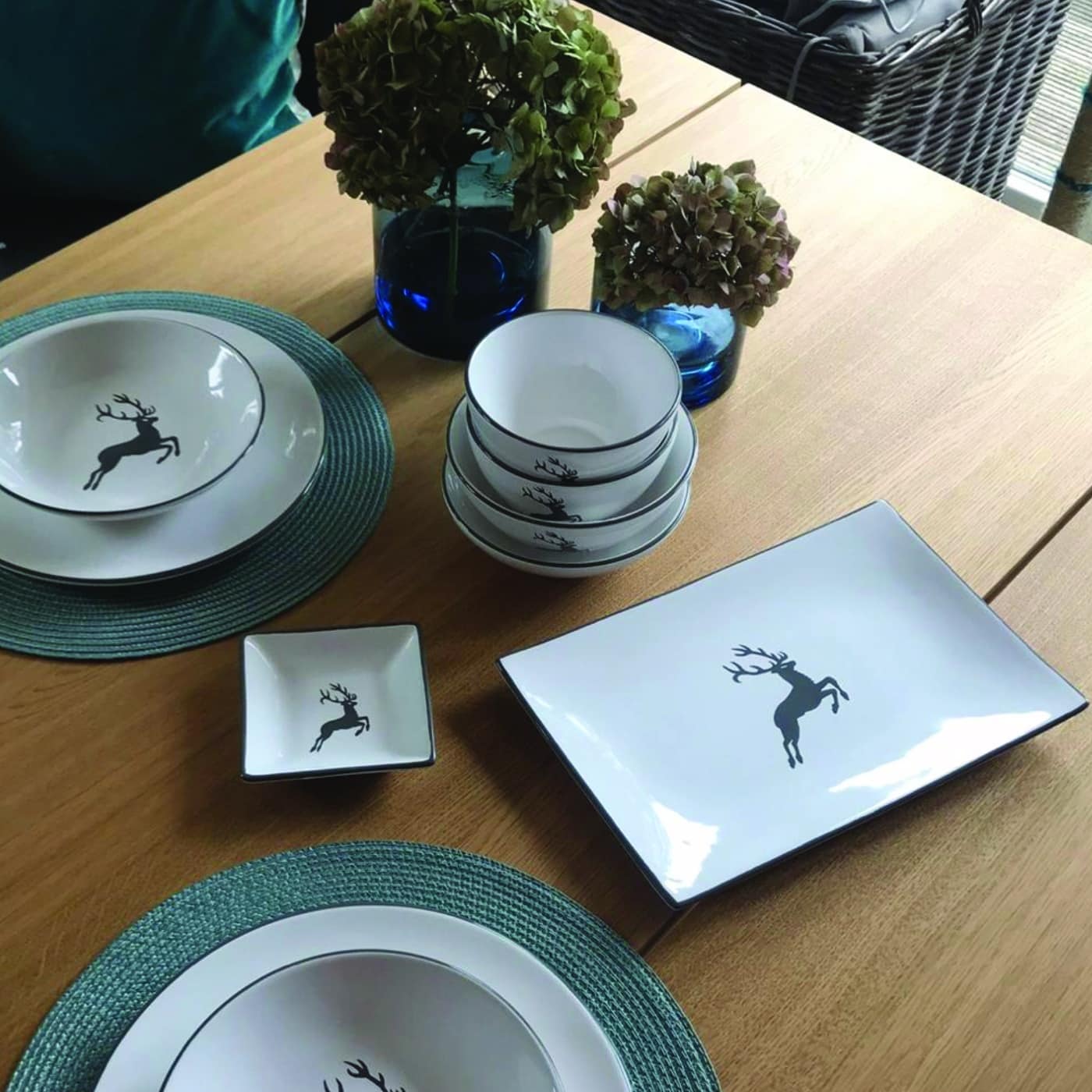 Gedeckter Eichenholztisch mit Geschirr im Hirschdesign und blauer Tischdekoration.