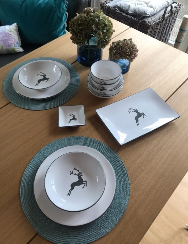 Gedeckter Eichenholztisch mit Geschirr im Hirschdesign und blauer Tischdekoration.