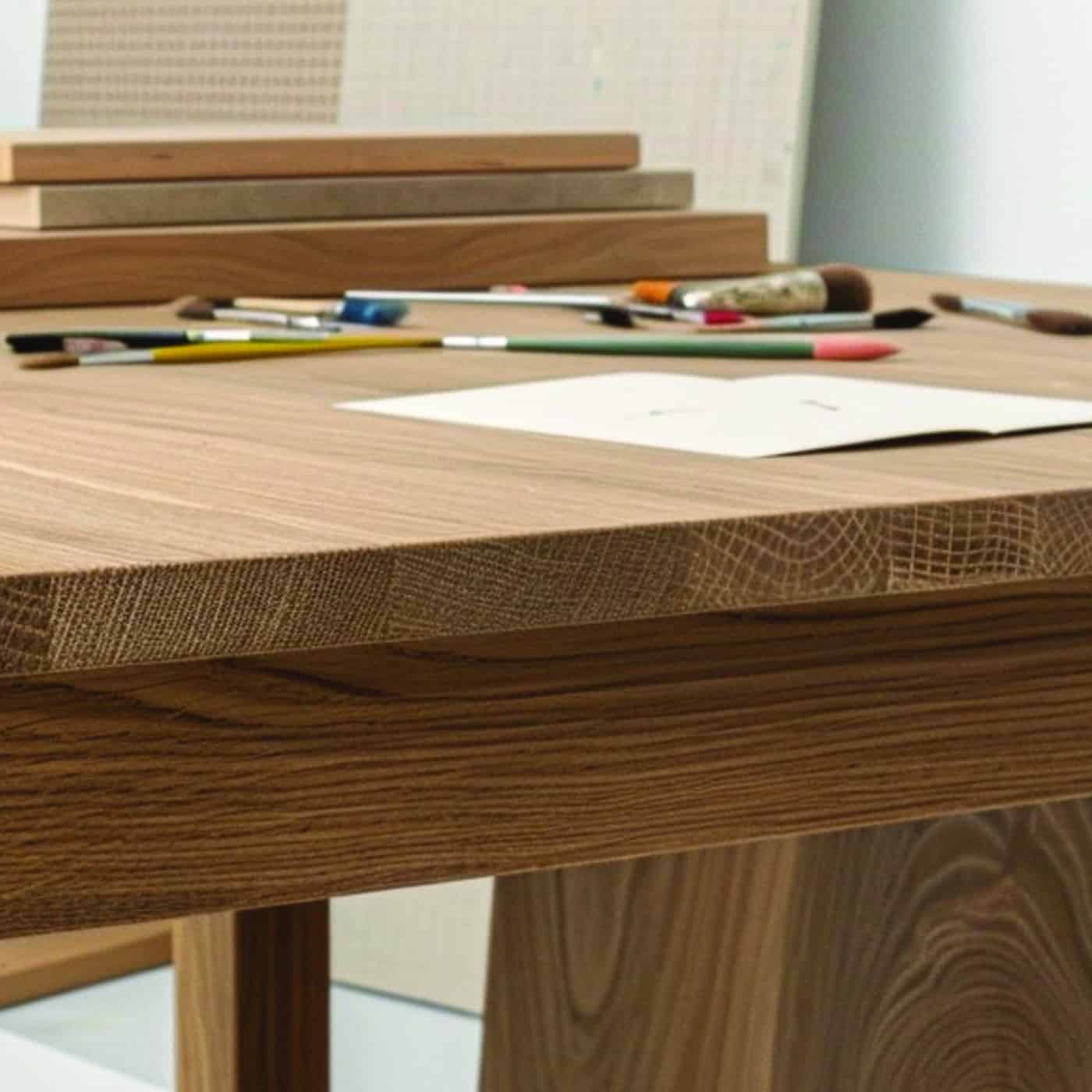 Nahaufnahme eines massiven Eichentisches mit Papier, Stiften und Pinseln auf der Oberfläche.