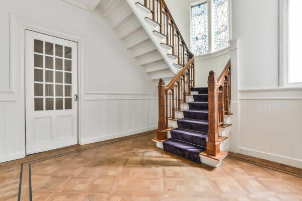 Eine Holztreppe führt durch einen hellen Eingangsbereich mit Parkettboden.