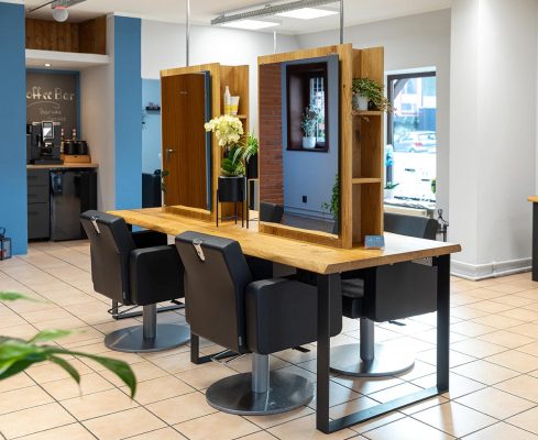Friseursalon mit Holzstylingtischen, schwarzen Stühlen und Pflanzen an den Spiegeln.