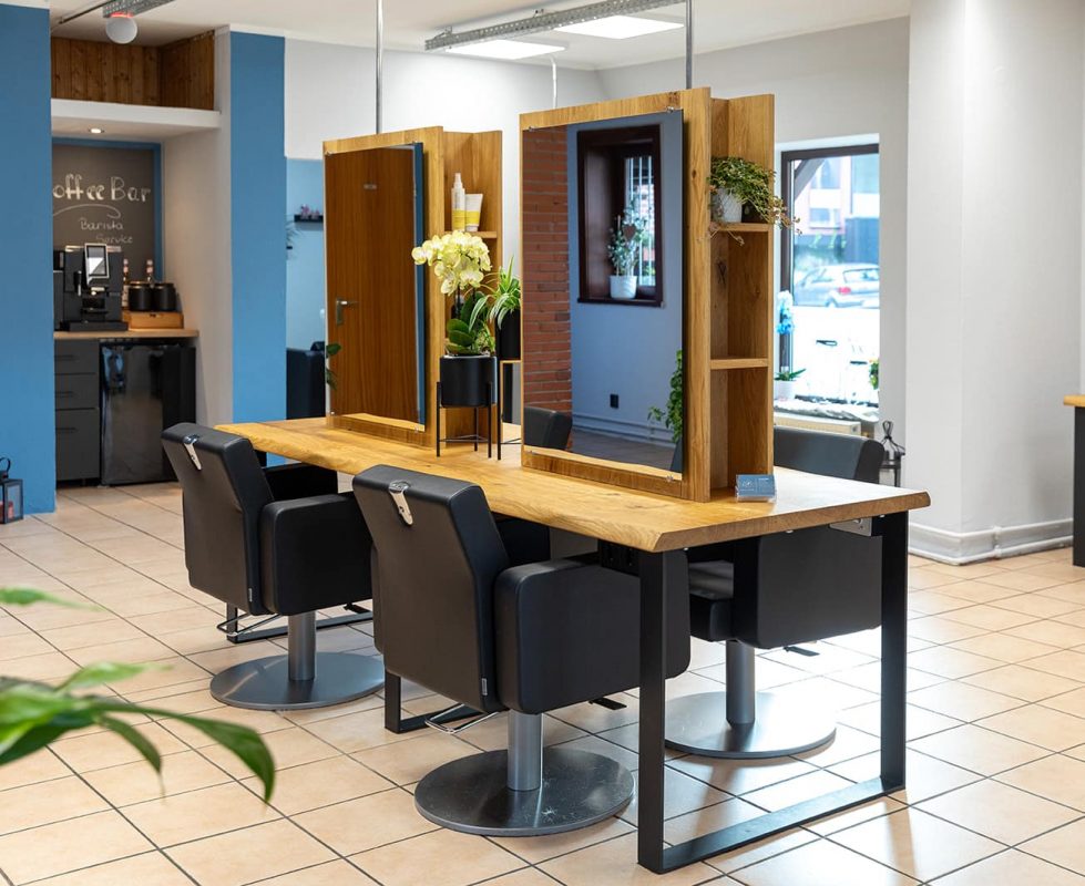 Friseursalon mit Holzstylingtischen, schwarzen Stühlen und Pflanzen an den Spiegeln.
