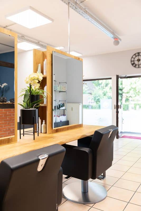 Ein moderner Stylingplatz mit Holzspiegel und schwarzen Friseurstühlen in einem Friseursalon.