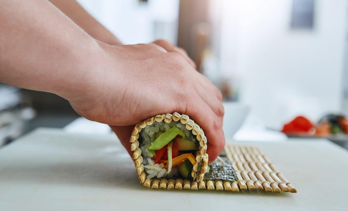 Sushirolle wird mit Bambusmatte sorgfältig geformt.