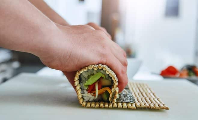 Sushirolle wird mit Bambusmatte sorgfältig geformt.