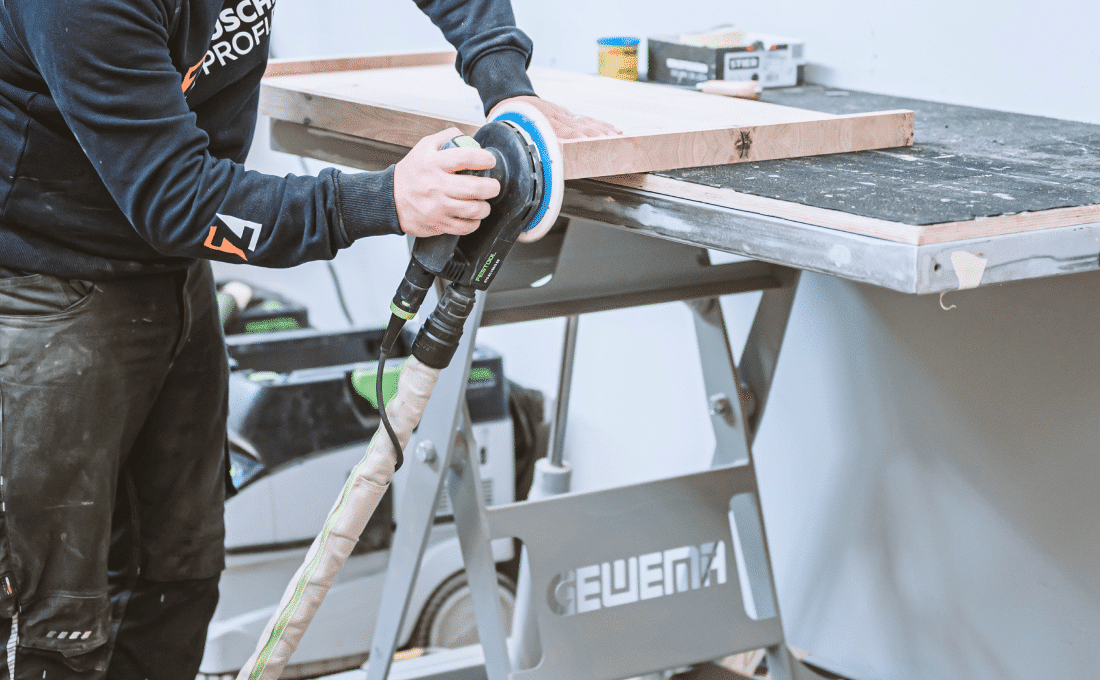 Ein Handwerker schleift eine Holzplatte mit einer Schleifmaschine.