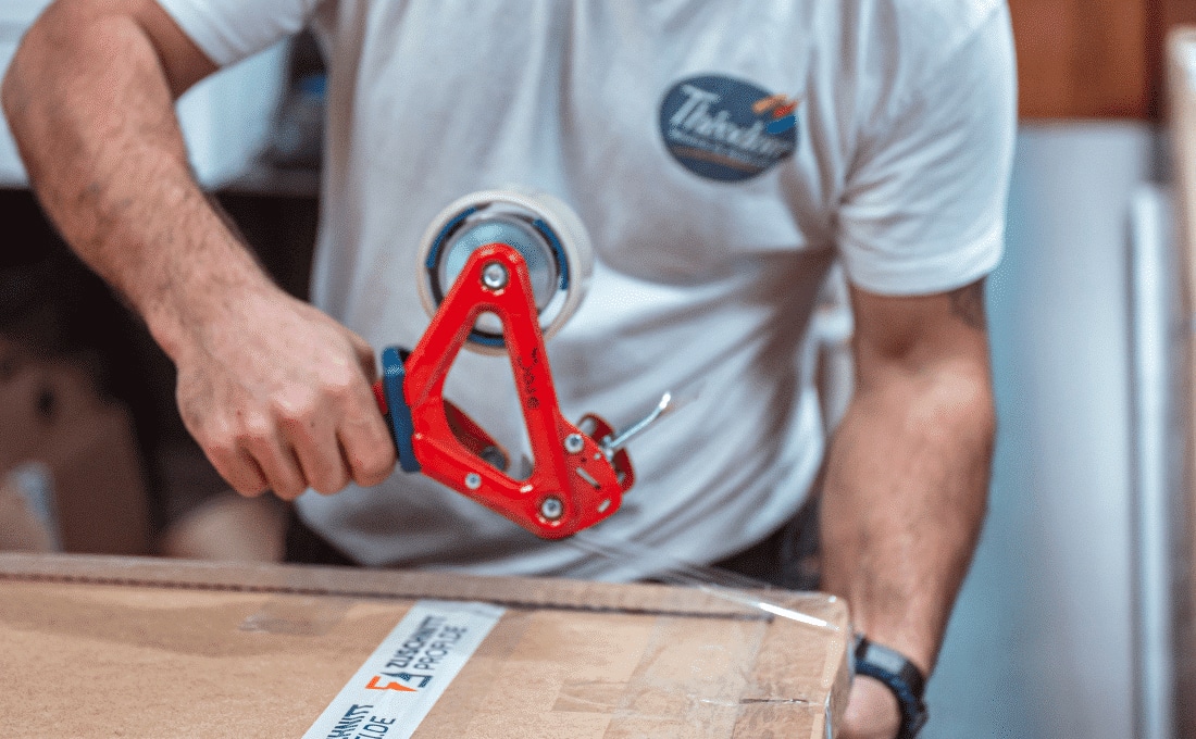 Ein Mitarbeiter verschließt ein Paket sorgfältig mit einem roten Handabroller.