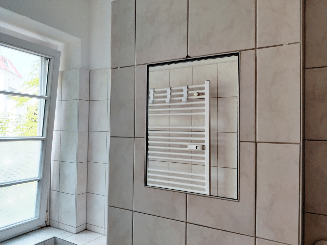 Ein Badspiegel hängt bündig an einer hell gefliesten Wand.