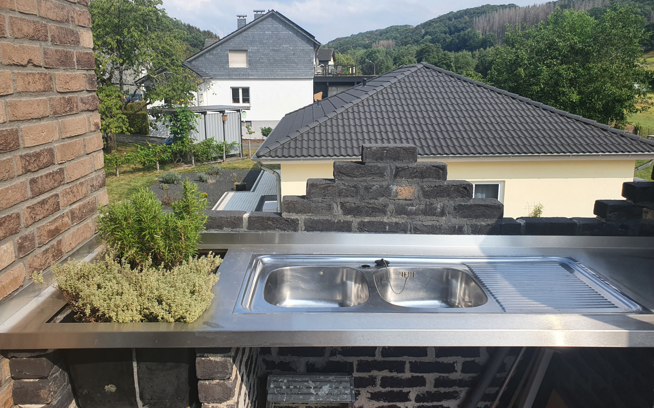 Eine Edelstahl-Außenküche mit Doppelspüle ist fest in eine gemauerte Terrasse integriert.