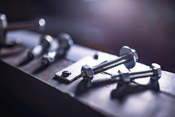 Mehrere Schrauben und Muttern liegen geordnet auf einer Metallplatte bereit.
