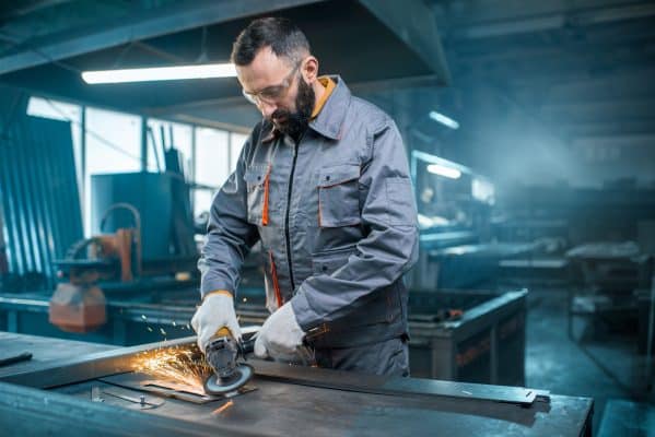 Ein Metallarbeiter schleift eine Stahlplatte in einer industriellen Werkhalle.
