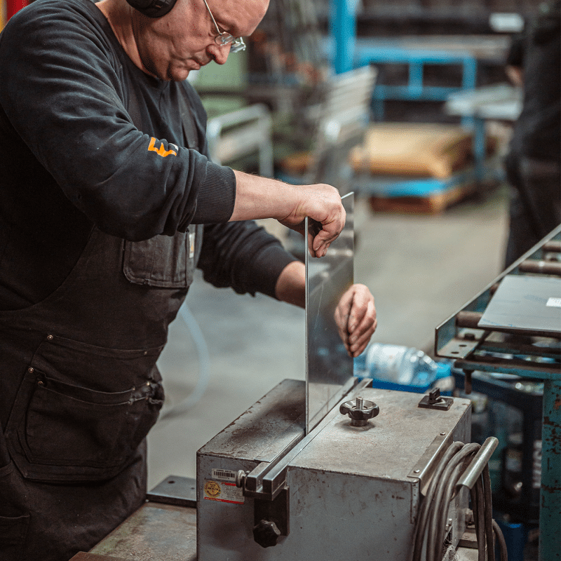 Ein Mitarbeiter bearbeitet ein Metallteil an einer stationären Maschine.