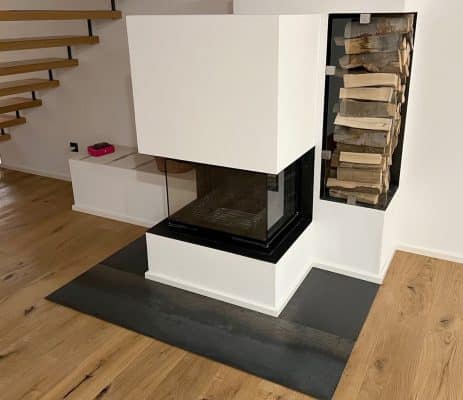 Ein Kaminbereich zeigt eine große Glasfront und eine dunkle Bodenplatte.