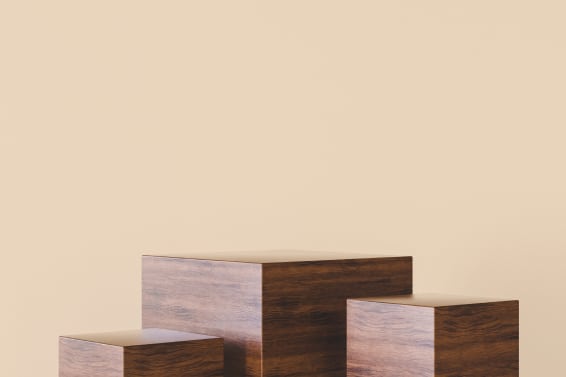 Drei würfelförmige Sitzboxen aus dunklem Holz vor beiger Wand.