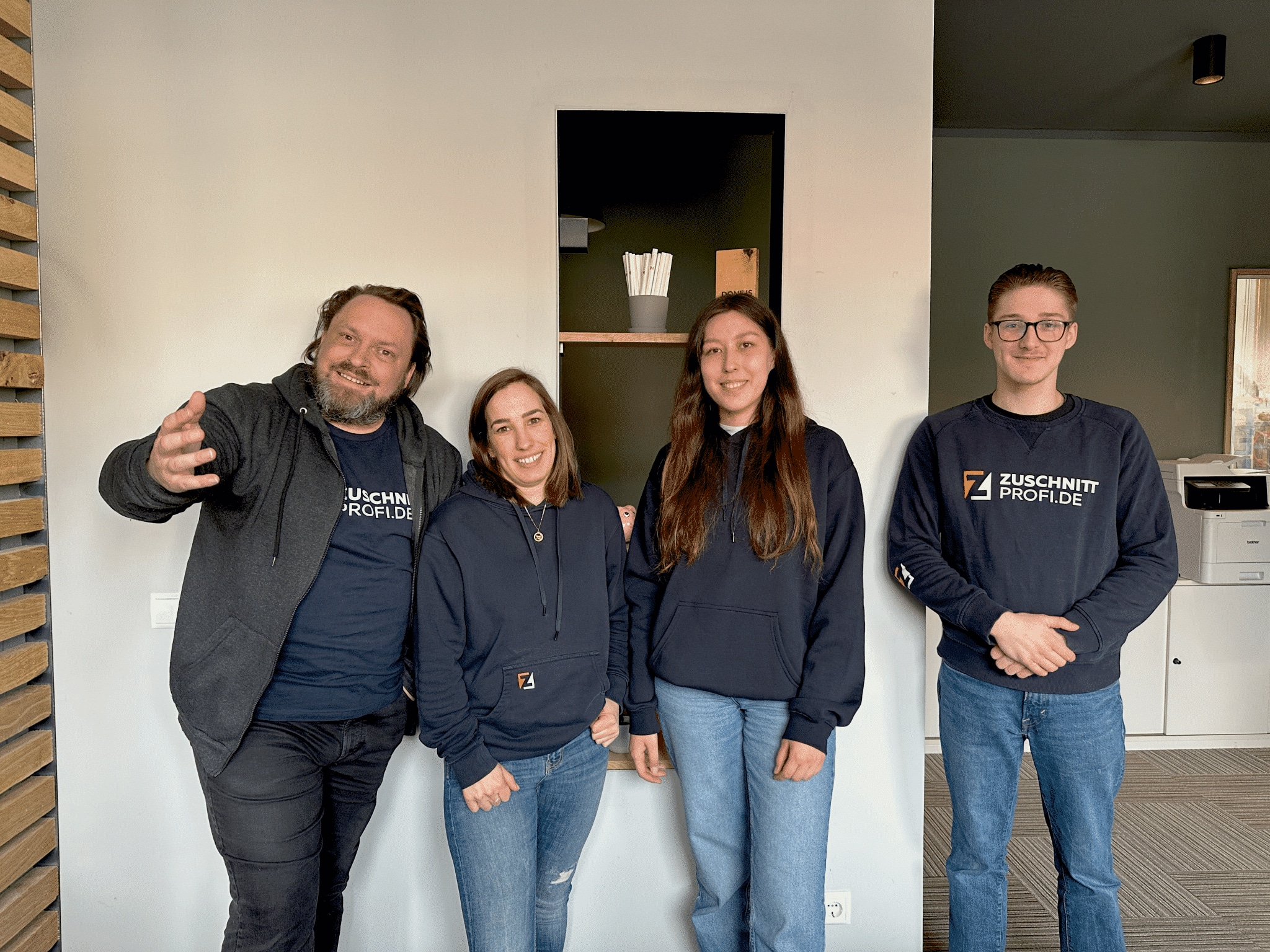 Ein Team von vier Personen von zuschnittprofi.mom steht freundlich im Bürobereich zusammen.
