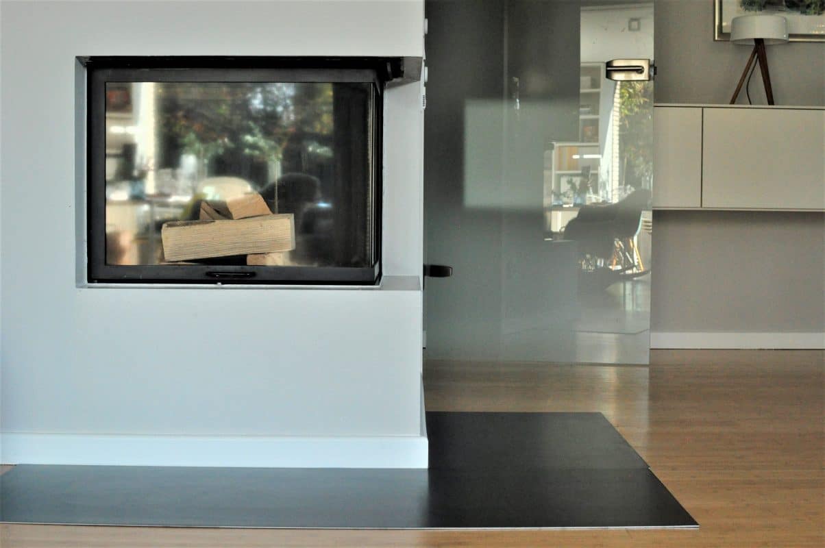 Kamin mit Holzscheiten und Glasfront in hellem Raum.