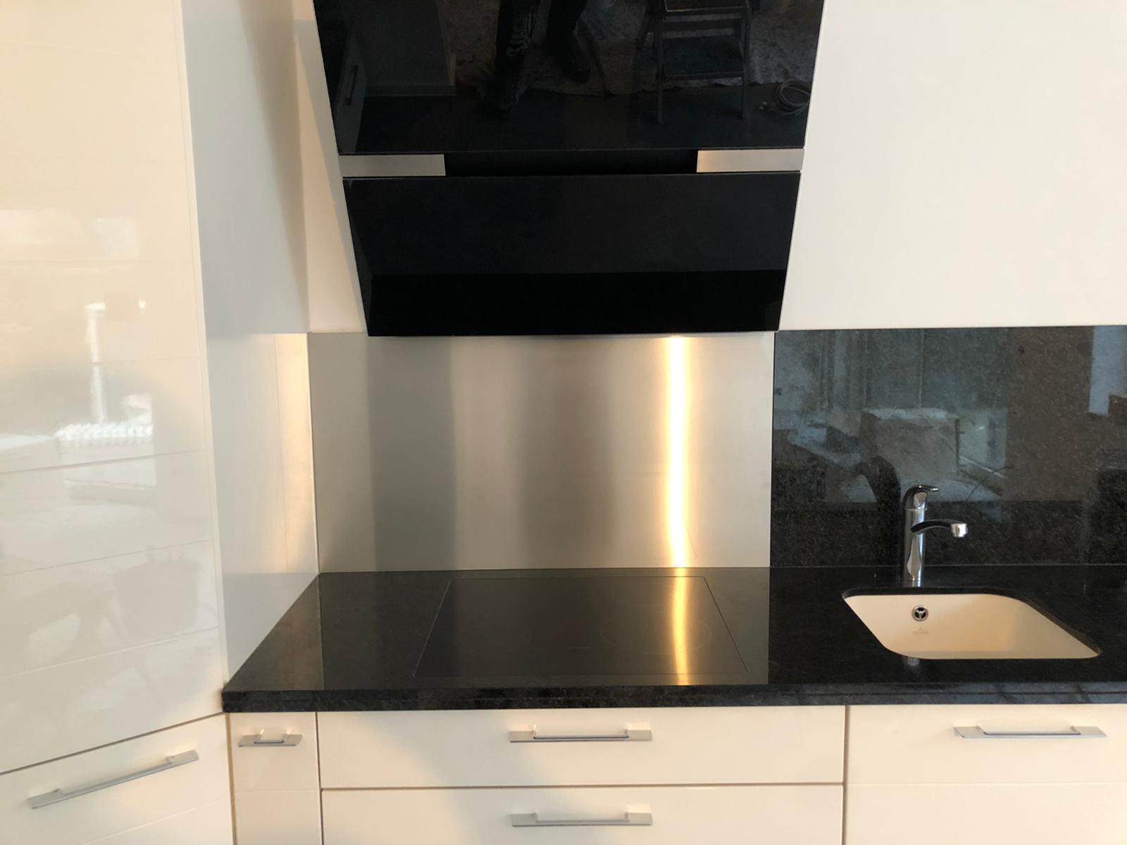 Eine glänzende Edelstahlrückwand reflektiert das Kochfeld und die Oberschränke.