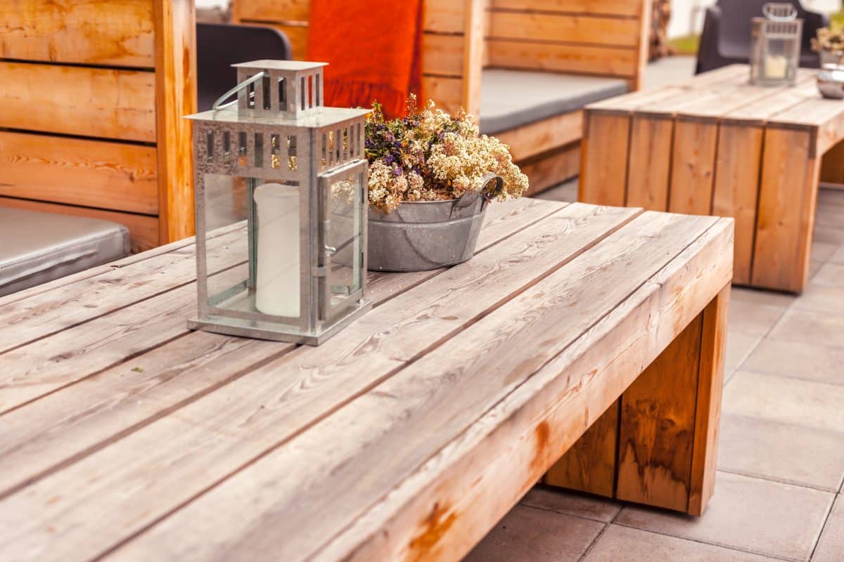 Holztisch auf Terrasse mit Laterne und Blumendeko.