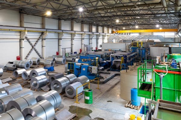 Eine Industriehalle zeigt Metallrollen und Maschinen in einer Produktionsumgebung.