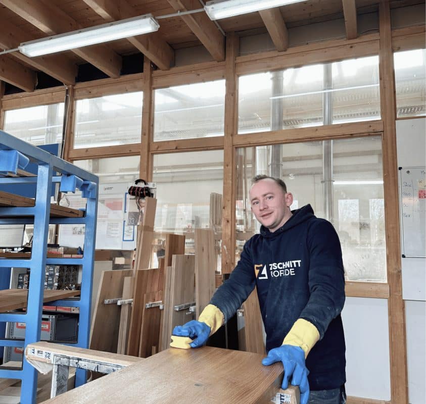 Ein Mitarbeiter von zuschnittprofi.mom richtet eine massive Holzplatte sorgfältig in der Werkstatt aus.