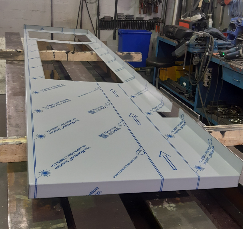 Zugeschnittene Metallplatten liegen geschützt auf einer Werkbank.