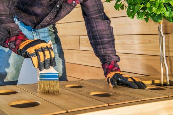 Eine Person ölt eine Holzplatte mit mehreren runden Aussparungen.