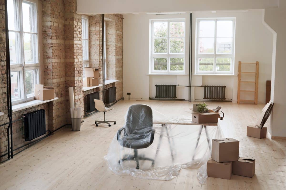 Interieur eines modernen Büroraums mit Backsteinwand und Büromöbeln unter Polyethylen während der Renovierung.