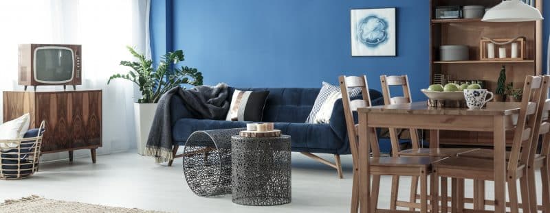 Ein Wohnzimmer zeigt ein Sofa, Beistelltische und eine blaue Wand.