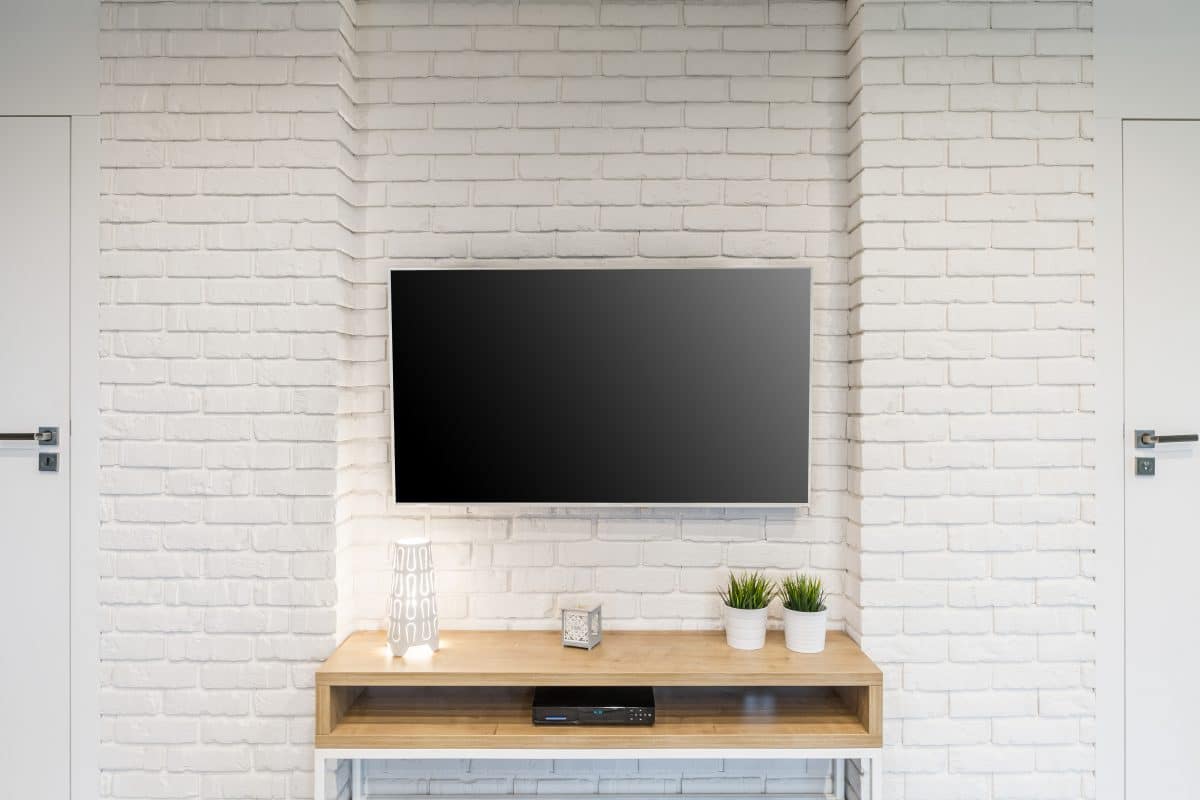 TV-Wand mit weißer Ziegeloptik und schlichtem Holzboard.
