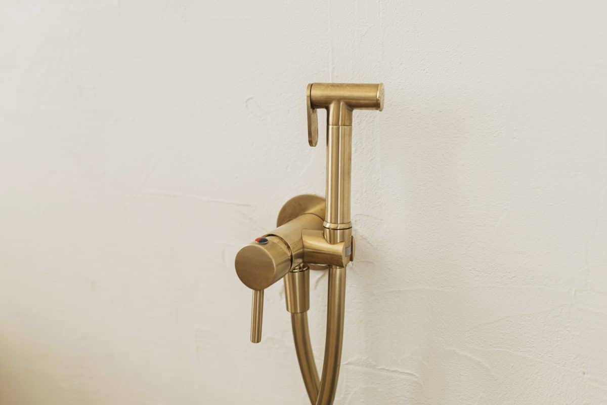 Goldfarbene Duscharmatur mit Handbrause an weißer Wand.