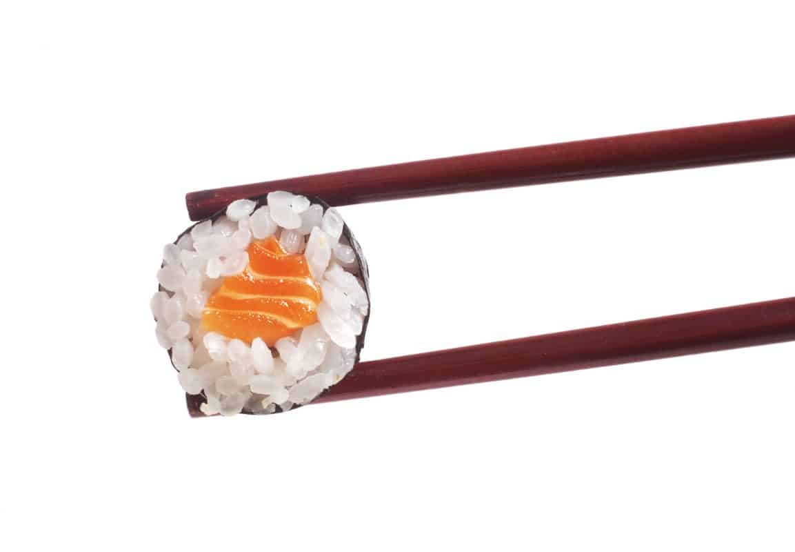 Sushi-Makirolle mit Lachsfüllung wird von Essstäbchen gehalten.
