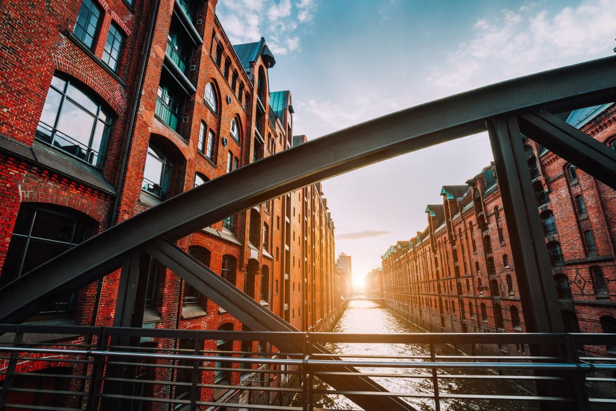 Das rote Backsteinlagerhaus, Speicherstadt in Hamburg in Deutschland, eingerahmt von Stahlbrückenbögen mit Kanalperspektive, erfüllt von warmem Sonnenuntergangslicht.