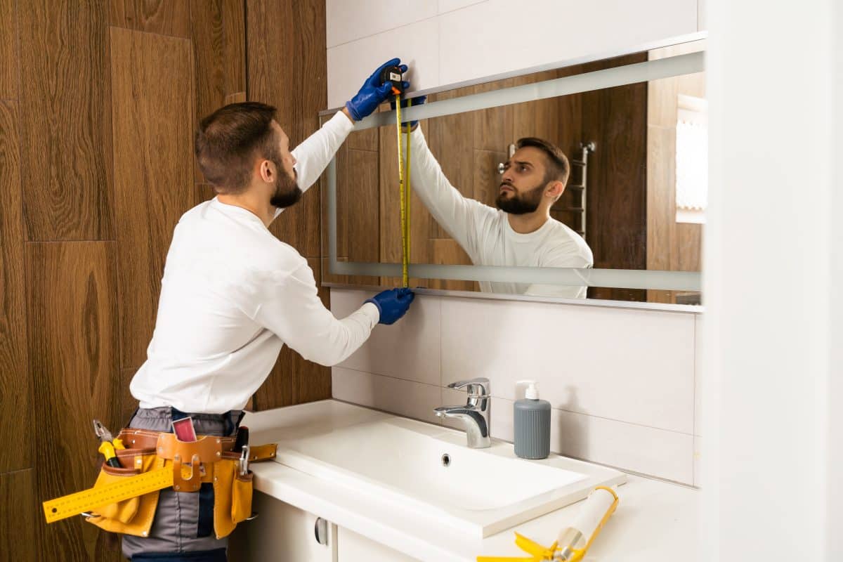 Ein Handwerker installiert einen Spiegel in einem Badezimmer. 