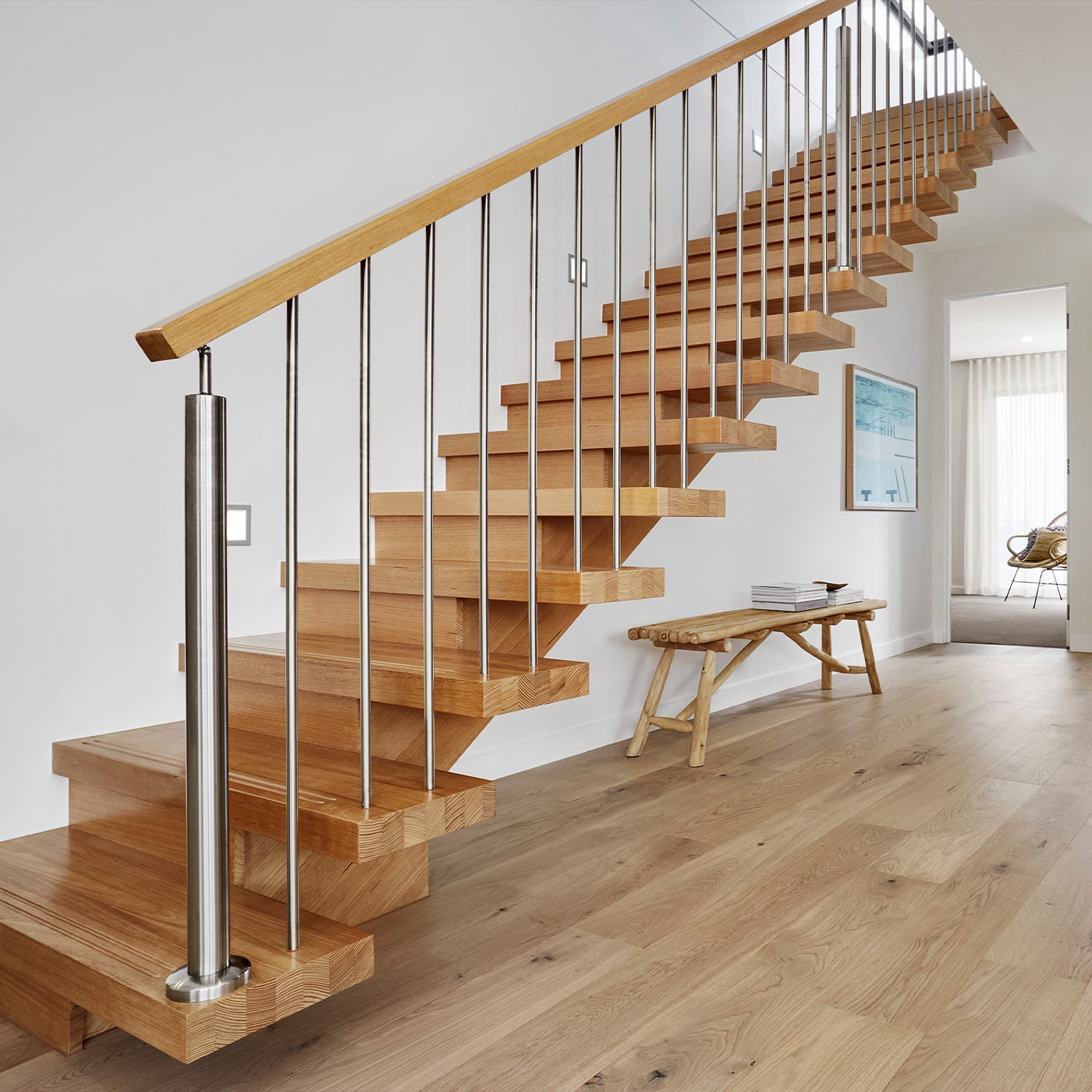 Eine moderne Holztreppe mit Edelstahlgeländer steht in einem hellen Wohnbereich.