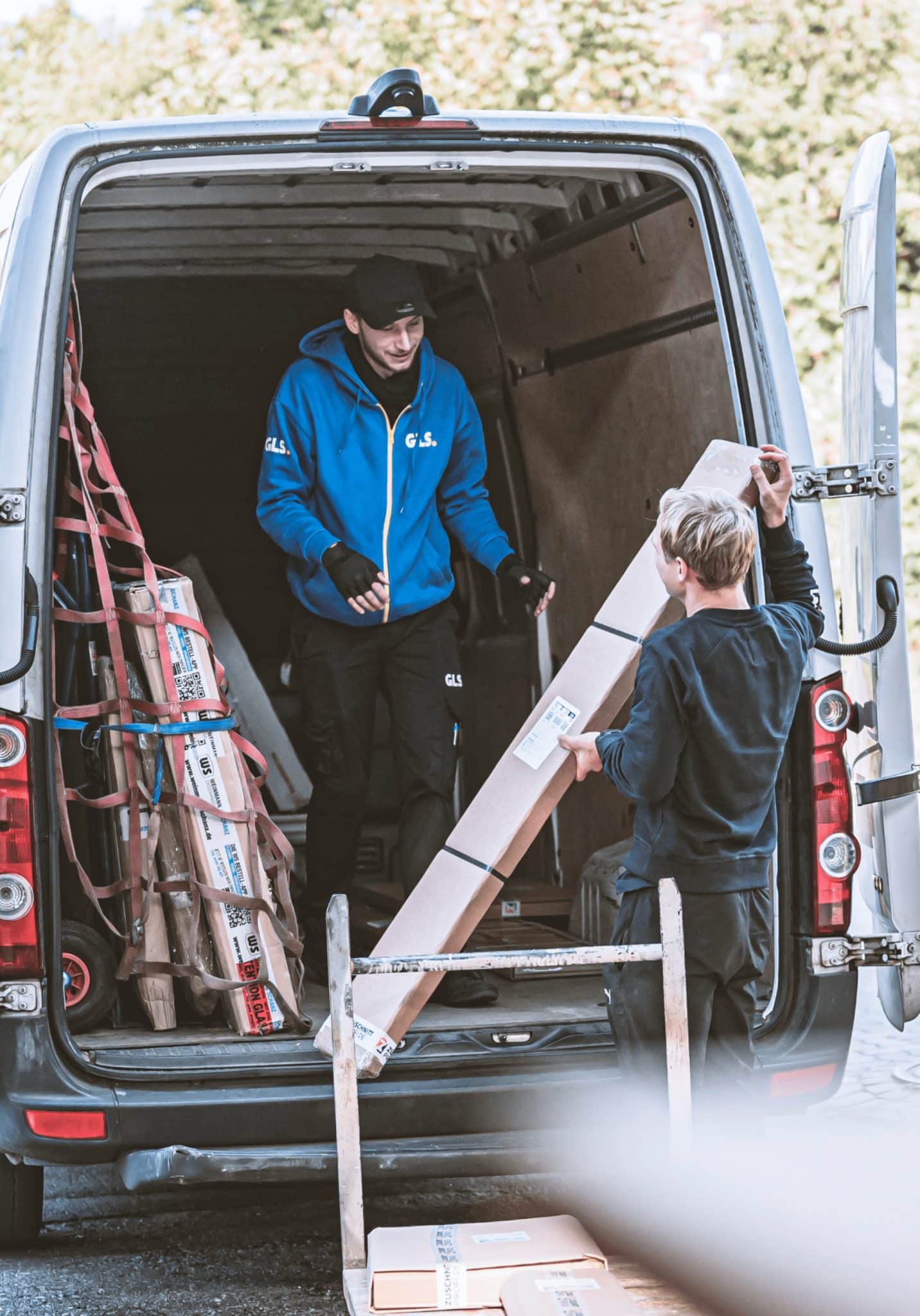Zwei Mitarbeiter von zuschnittprofi.mom laden Material in einen geöffneten Transporter.