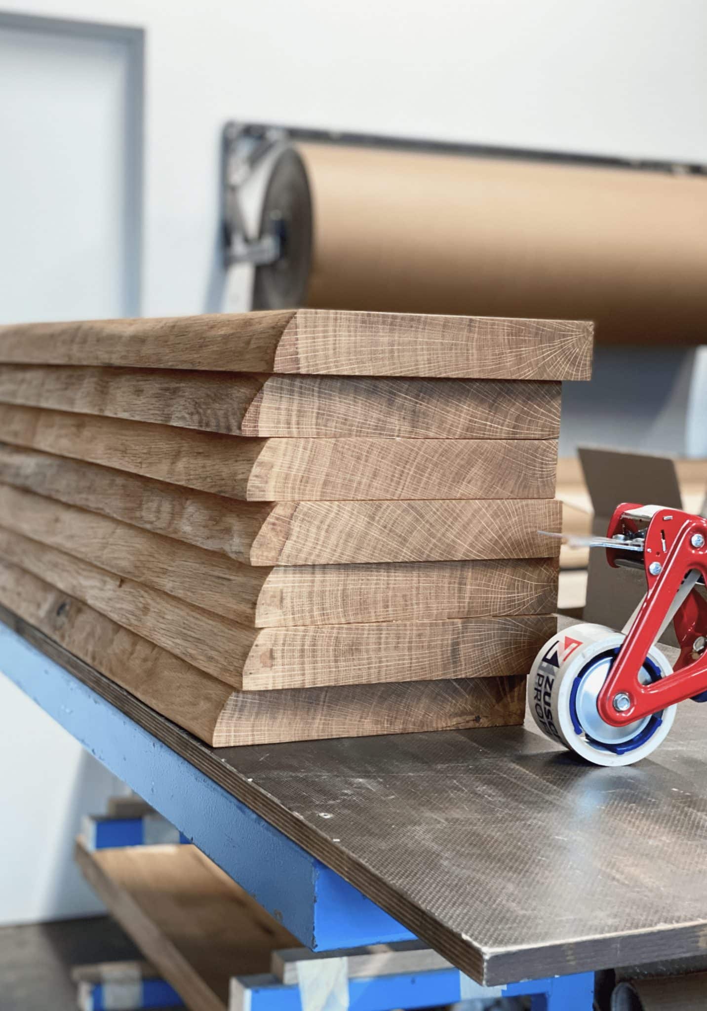 Mehrere massive Holzbohlen liegen ordentlich gestapelt auf einem Arbeitstisch.