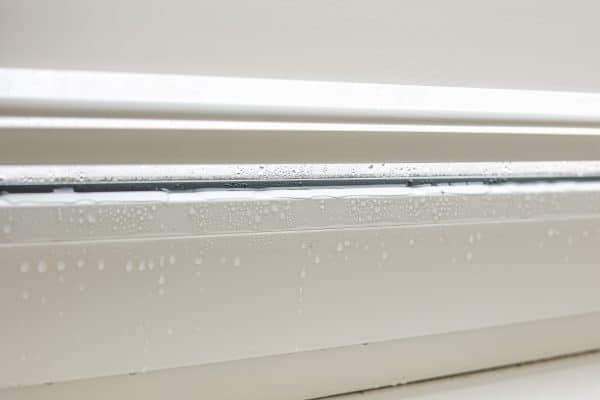 Wassertropfen sammeln sich auf einer weißen Fensterkante.