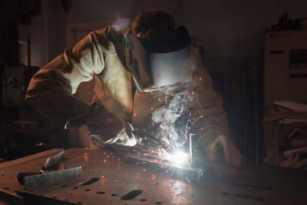 Ein Schweißer verbindet Metallteile mit Schutzhelm und Funkenflug.