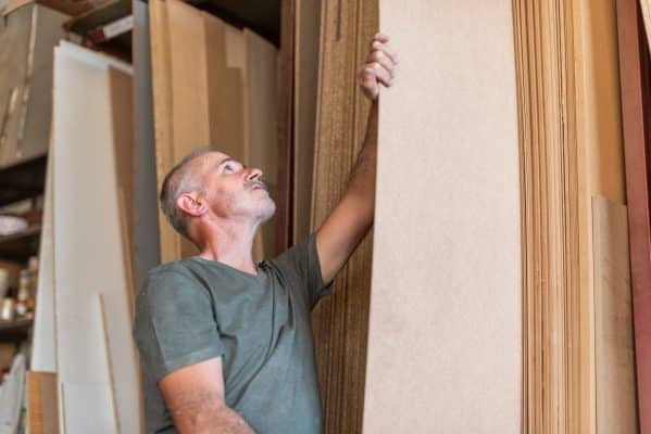 Ein Mann ordnet eine Holzplatte in eine Ablage in einer Werkstatt ein.